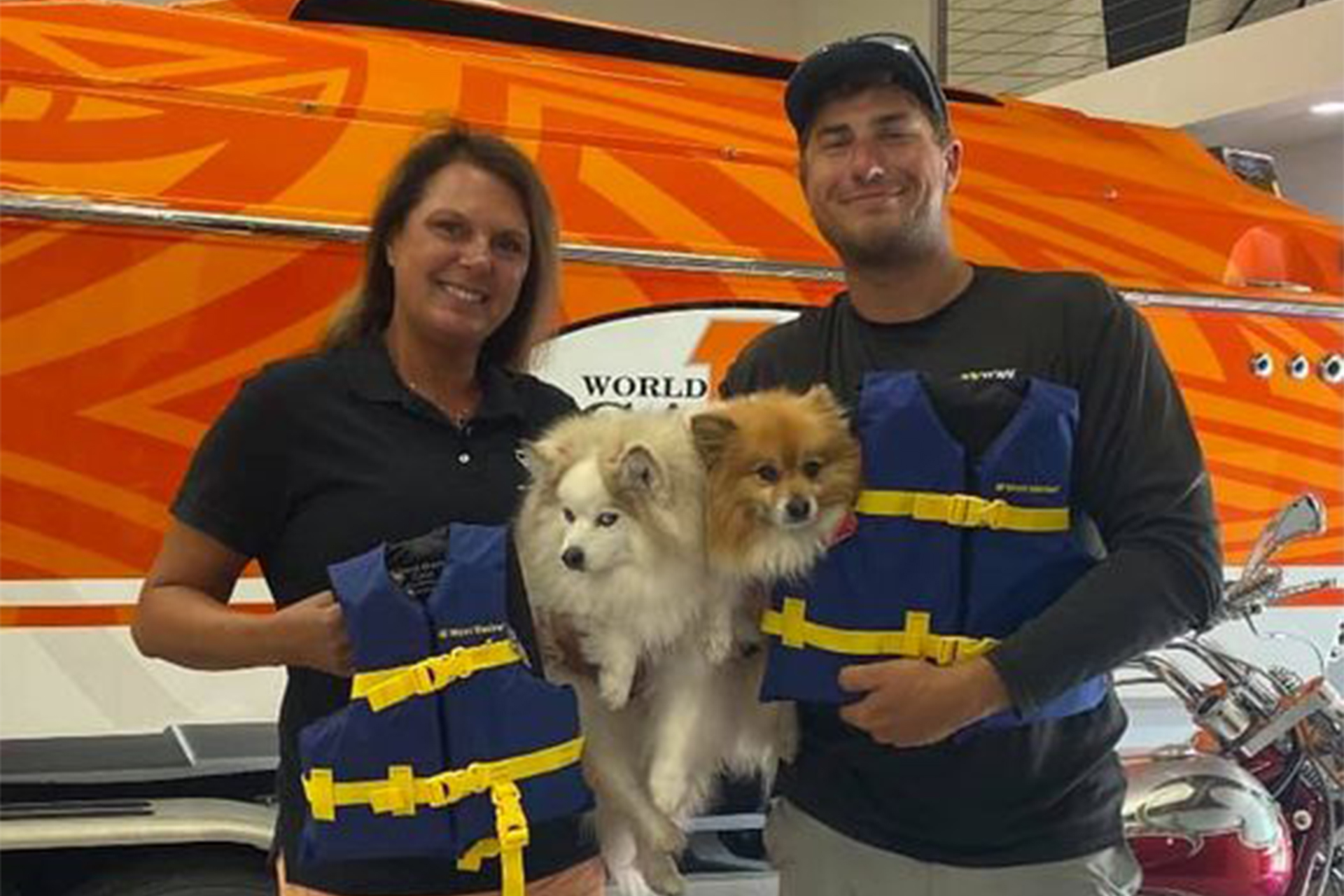 Couple in front of custom boat; holding two dogs.